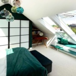 Modern attic bedroom with green and white decor, sloped ceiling, large skylight windows, built-in window seat, and pendant lighting.
