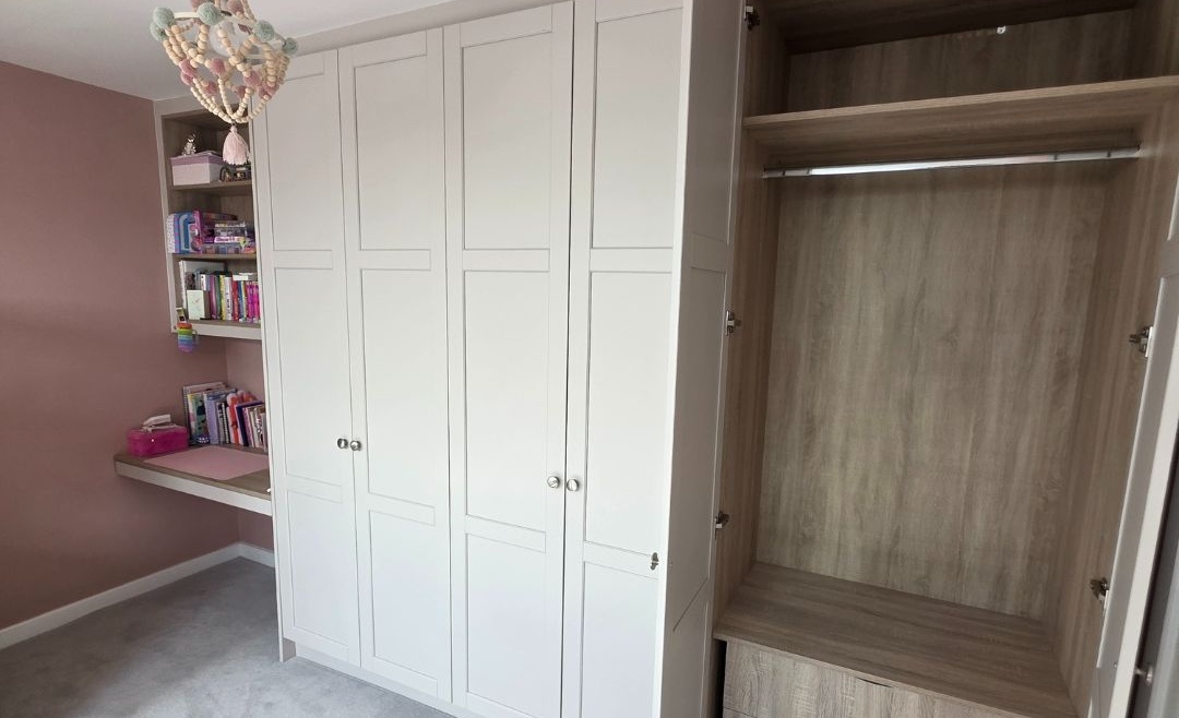 Fitted attic wardrobe with open doors and integrated shelving in a pink attic bedroom