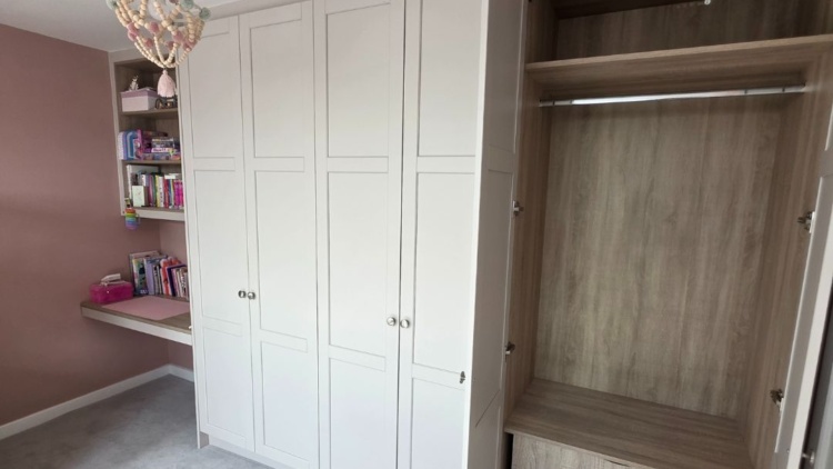 Fitted attic wardrobe with open doors and integrated shelving in a pink attic bedroom