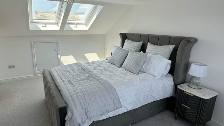 Modern attic bedroom with grey carpet, large skylights, and a plush double bed—showcasing post-renovation comfort and natural light.